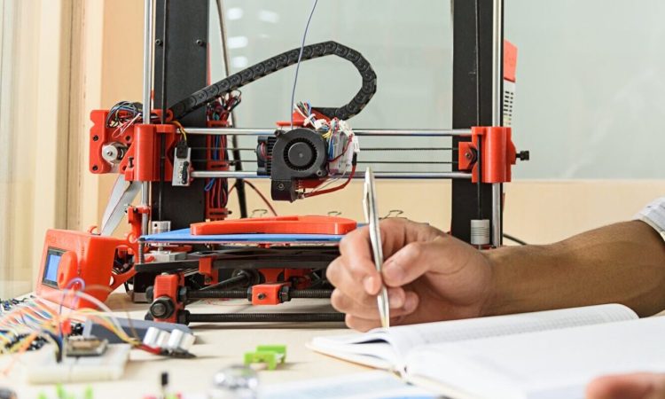 Happy young scientist glad about 3d printing This 3d printer is wonderful. Joyful male engineer is doing research in technology lab. He is sitting and making notes. Man is looking at camera and smiling